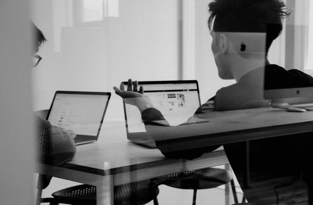 Two professionals discussing SEO strategy and comparing provider options on their laptops in an office